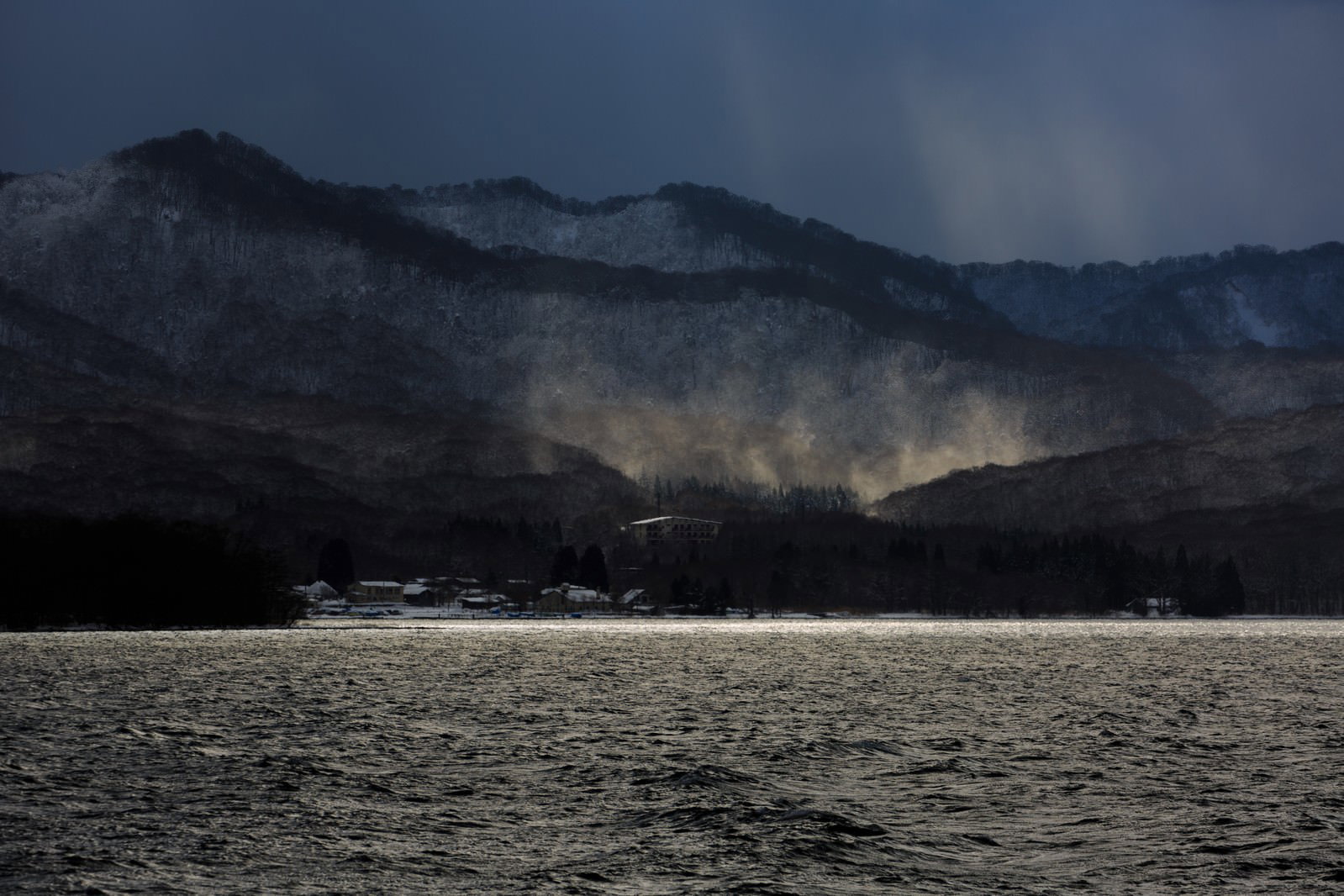 雪の積もった山々が湖の向こうに連なり、朝霧が立ちこめる冬の十和田湖