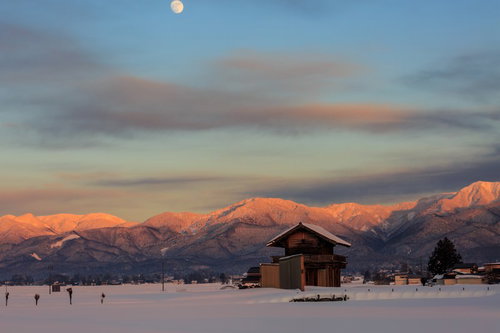 雪に包まれた奥羽山脈と昇る月、朝焼けに染まる冬の雪原風景