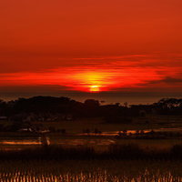 水平線に沈む真っ赤な日の入り、田園風景を照らす夕焼け空の写真