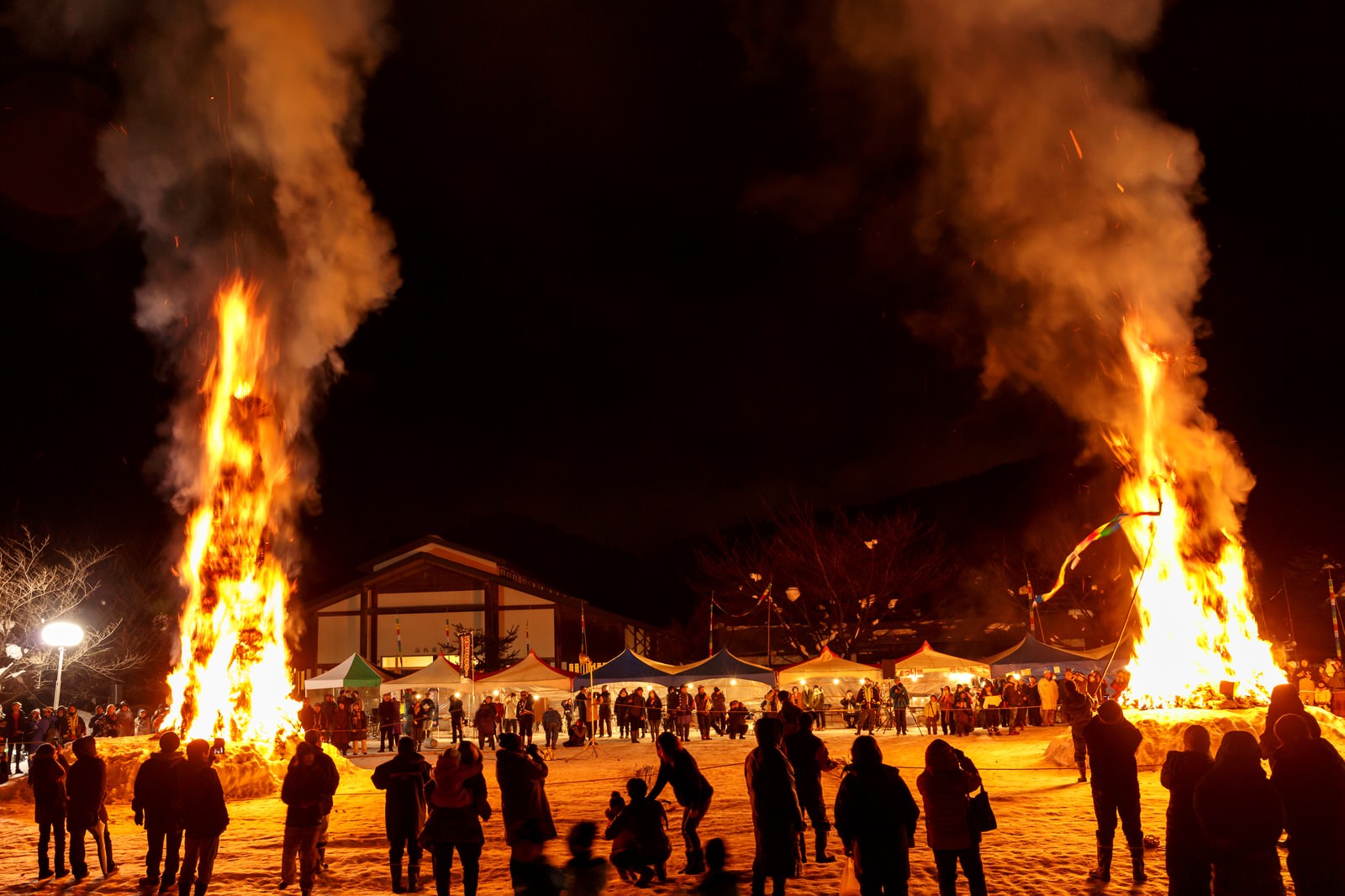夜空に燃え上がる2本の巨大な火柱と観衆のシルエット