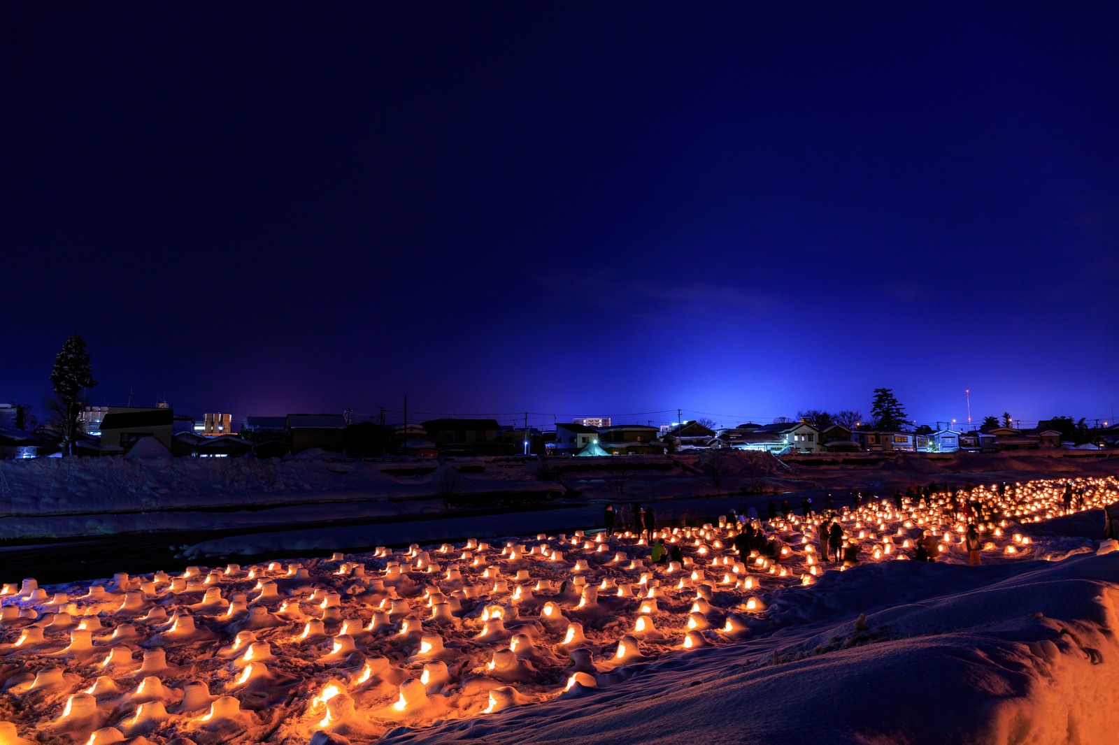 川沿いに並ぶ雪のミニかまくらが温かな灯りで照らされている夜景
