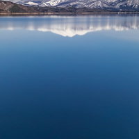 田沢湖面に映る雪の秋田駒ヶ岳と青空の水鏡風景の写真