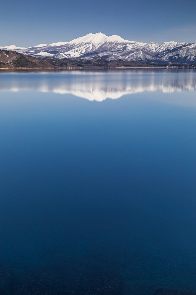 田沢湖の静かな湖面に雪をかぶった秋田駒ヶ岳が鏡のように映り込む風景