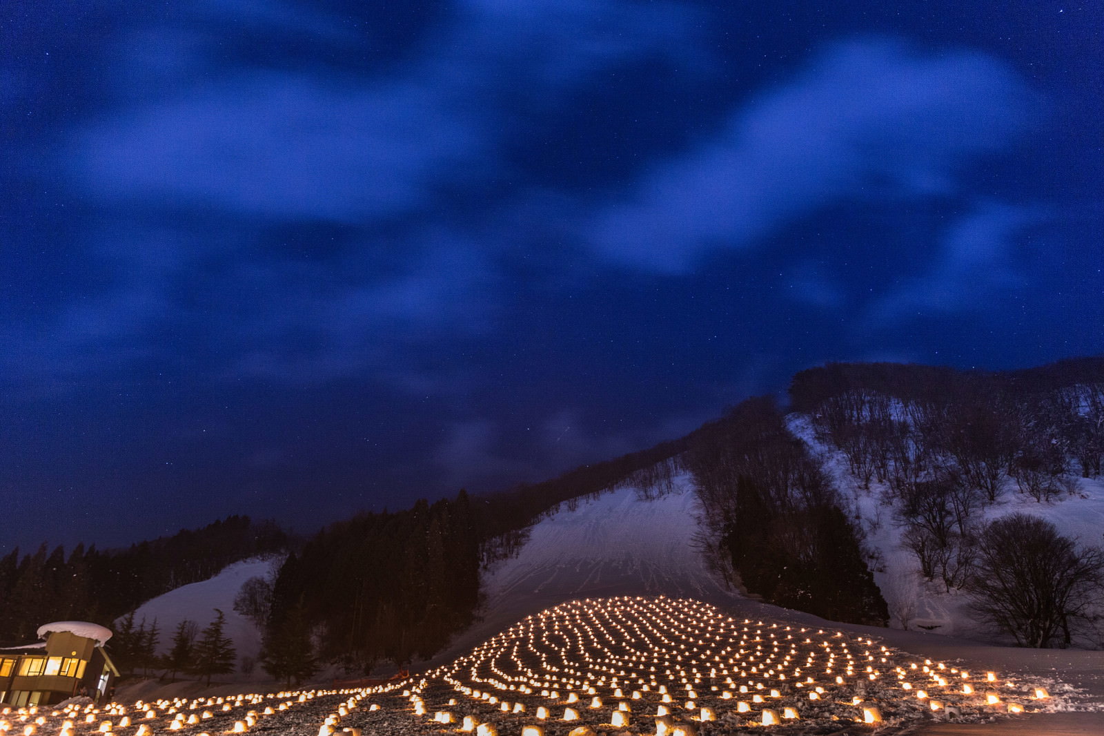 雪の斜面に灯籠が並ぶ冬祭りの夜景