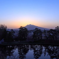 弘前公園から望む夕暮れの岩木山、池に映る樹木と空の色彩の写真