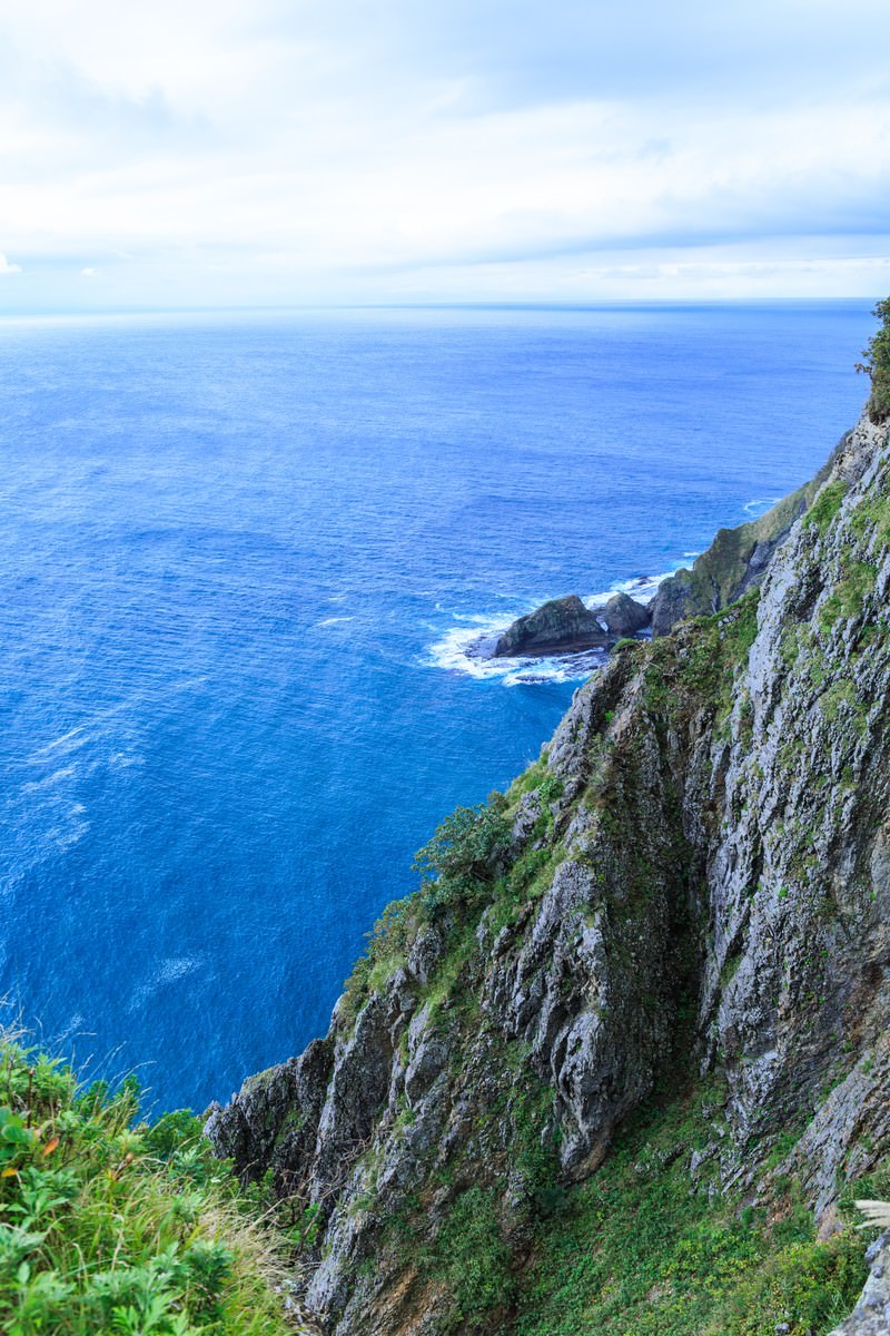 苔の生えた断崖絶壁の上から見下ろした青い海と岩礁に砕ける白波