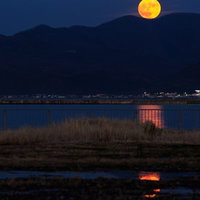 山の稜線から昇る満月と湖に映る月光の写真