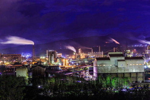 煙たなびく工場夜景の工業地帯、ライトアップされた夜間の製造プラント