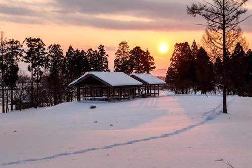 雪国の日没、森の中の茅葺き屋根の民家と夕焼け
