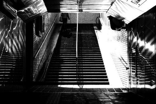 地下通路の階段をしょんぼり上る人（モノクロ）