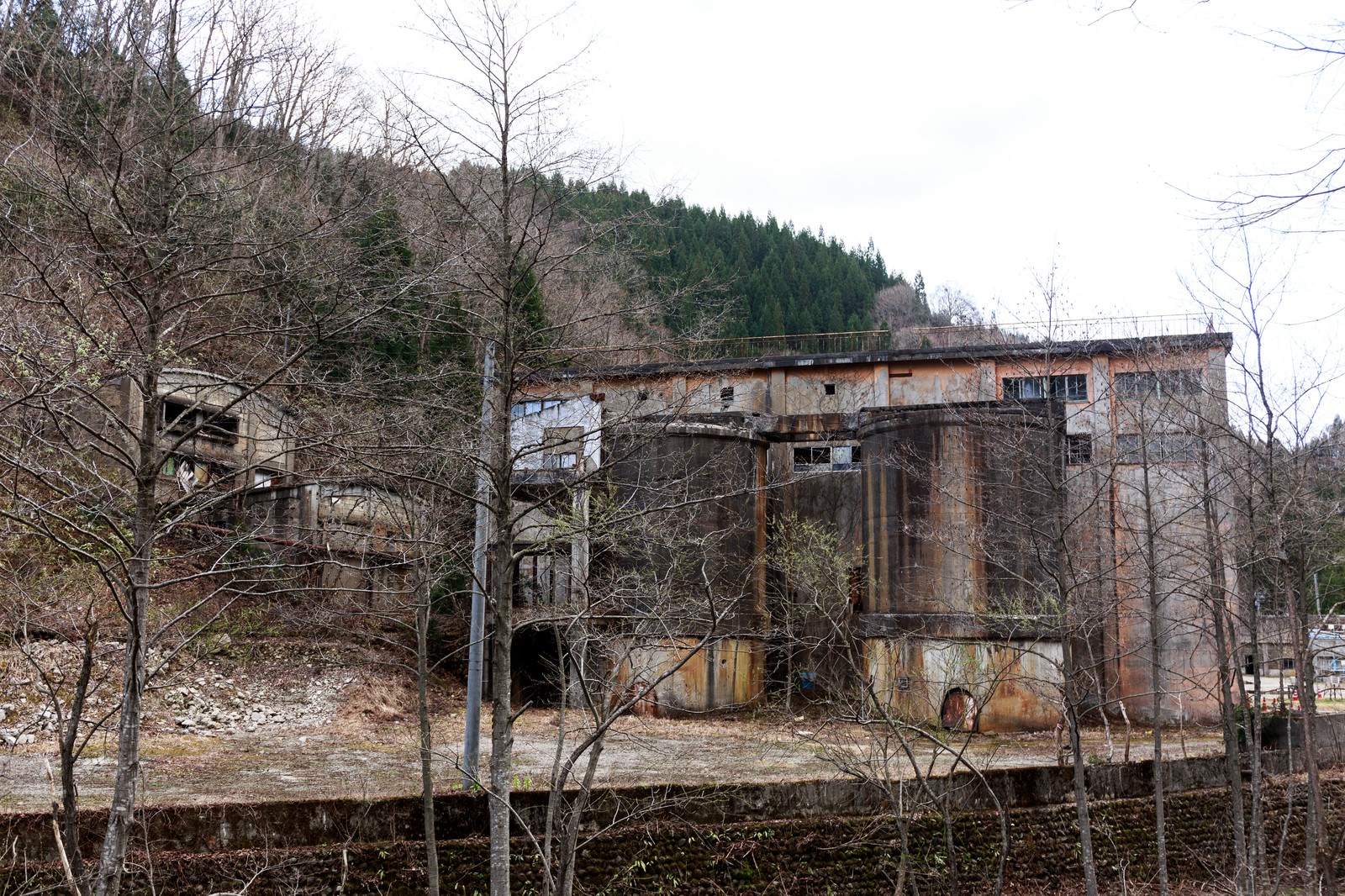 裸木に囲まれた古遠部鉱山跡の錆びた鉄骨と剥げた壁の廃墟建物