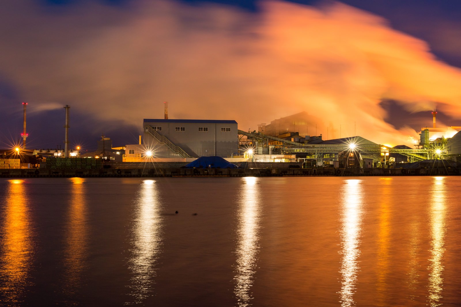 Night view of illuminated factory facilities in Hachinohe, with lighting reflected in the river and multiple smokestacks