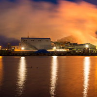 夜間にライトアップされた八戸工場夜景、川に映る光と煙突の写真
