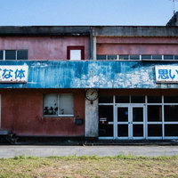 廃校となった赤い校舎の外観、青い錆びた看板と古い時計の写真