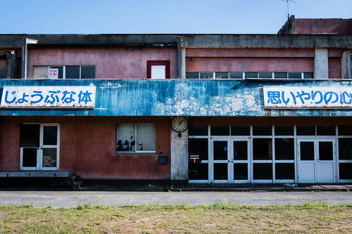 廃校となった赤い校舎の外観、青い錆びた看板と古い時計