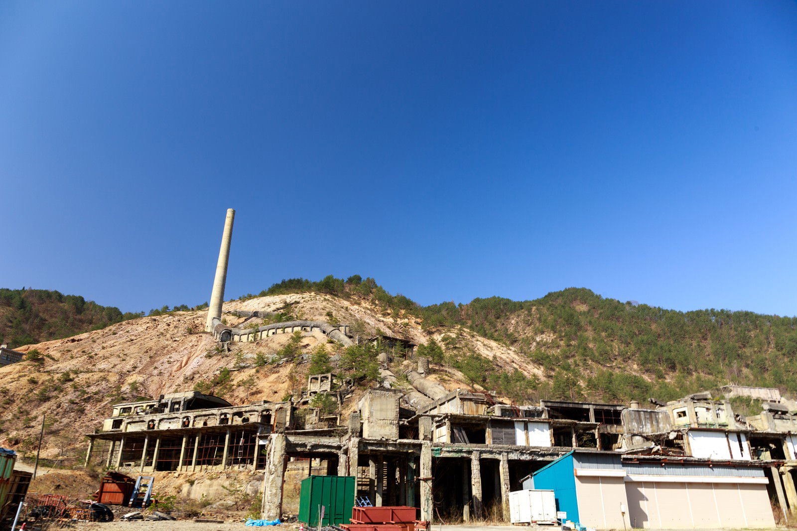 尾去沢鉱山跡の煙突と廃墟建物、露出した山肌と青空