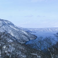 雪に覆われた冬の十和田湖と周囲の山々の風景の写真