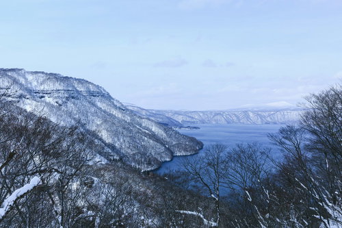 雪に覆われた冬の十和田湖と周囲の山々の風景