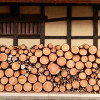 古民家の軒先に積まれた薪と黒い梁の建物の冬支度の写真