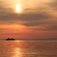 夕焼けの海に浮かぶ連絡フェリーと夕日の写真