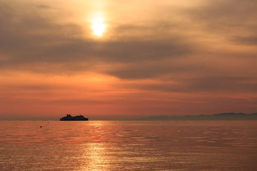 夕焼けの海に浮かぶ連絡フェリーと夕日
