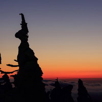 夕暮れの山頂に立つ樹氷のシルエット、赤橙色から紫へのグラデーションの写真