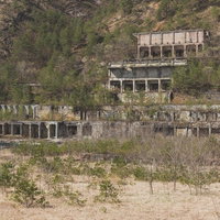 樹木で覆われた尾去沢鉱山跡の廃墟、石造りと鉄骨の複数階層建物の写真
