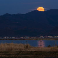 山並みに昇るスーパームーン 水面に映る月光の写真