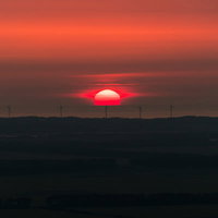 風力発電所の地平線に沈む夕日と風車のシルエットの写真
