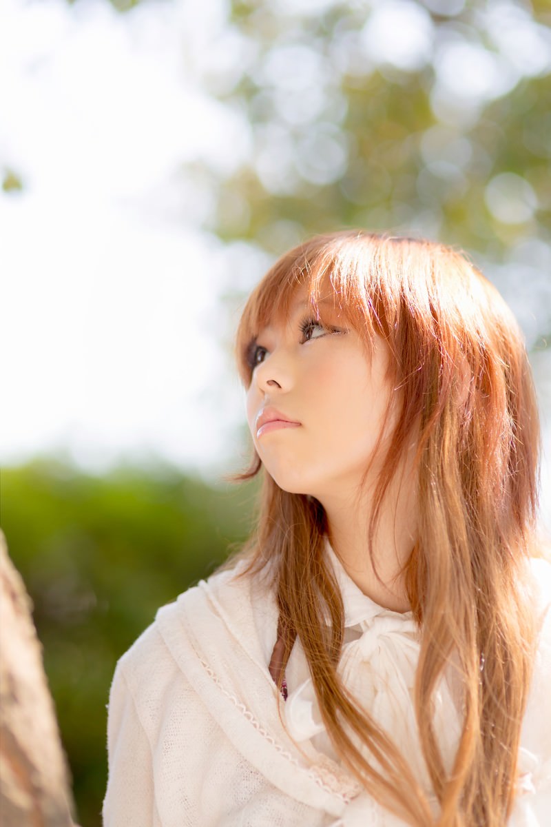 木陰で空を見上げる茶髪の女性がクローズアップで写っている［モデル：あみ］
