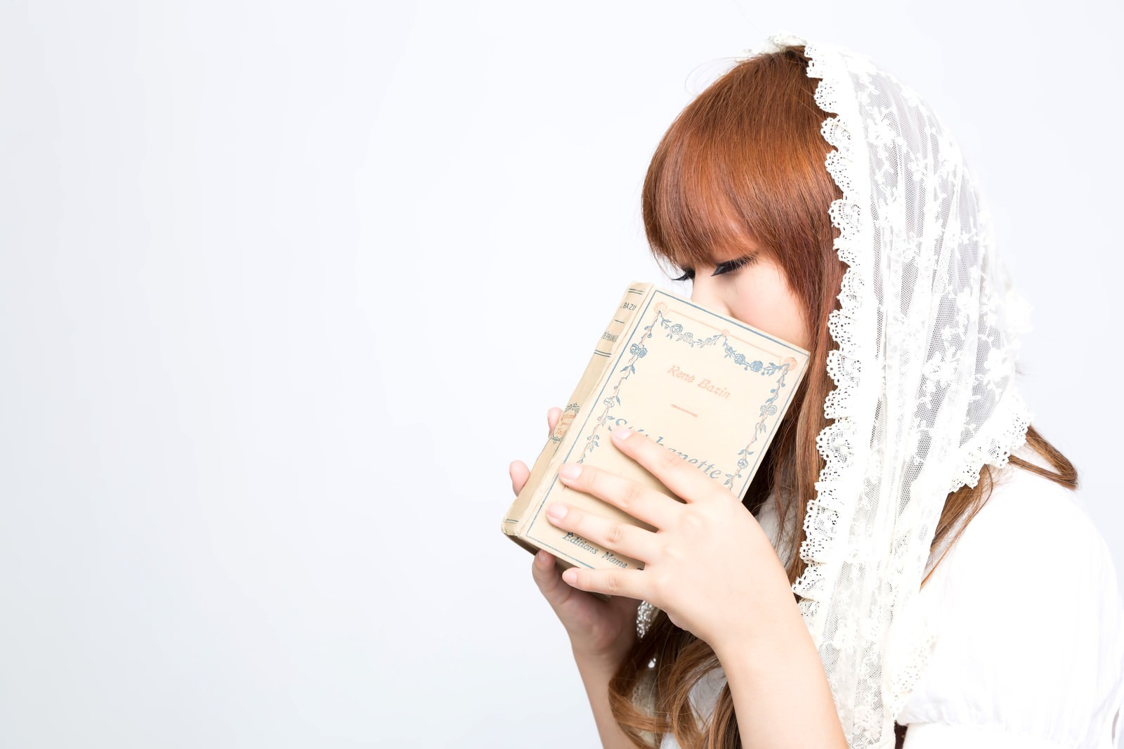 白いレース編みのベールをつけた女性が洋書で口元を隠している［モデル：あみ］
