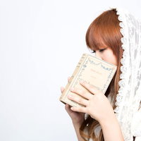 本で口元を隠すレース衣装の女性の写真