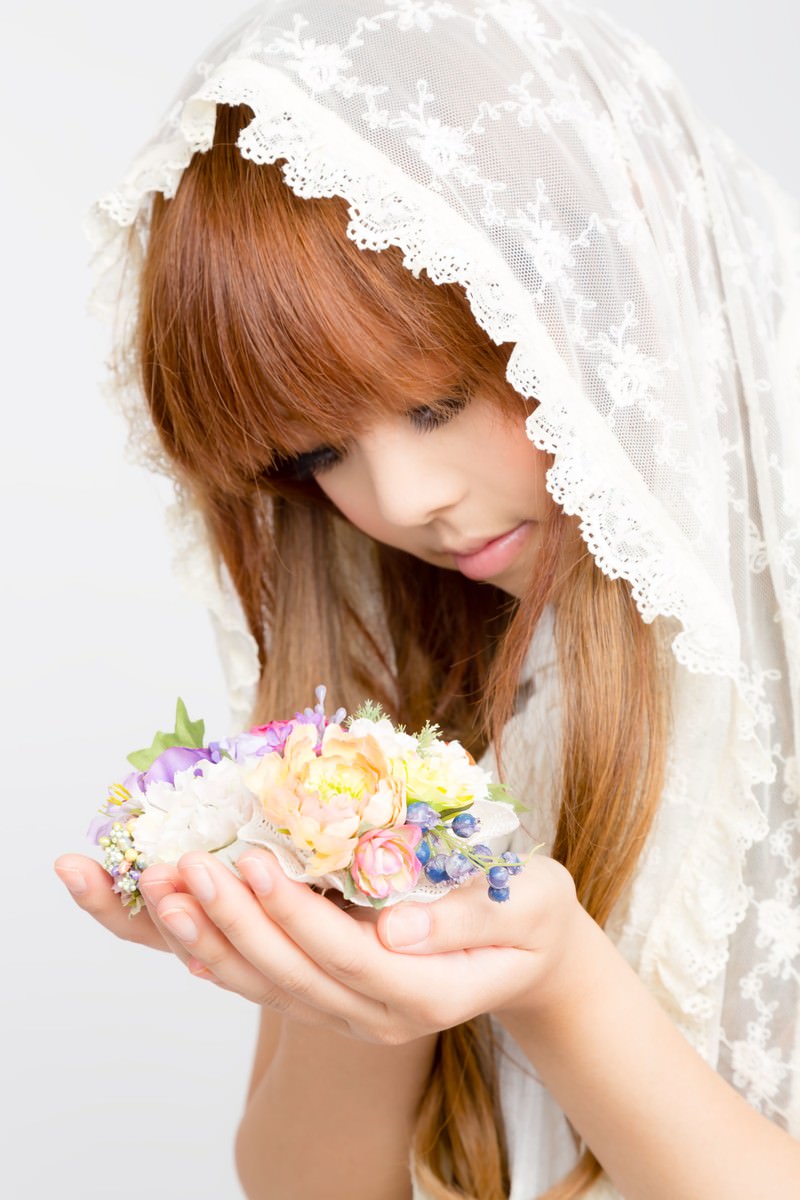 白いレース付きスカーフを被り、両手に造花の花束を持つ女性［モデル：あみ］