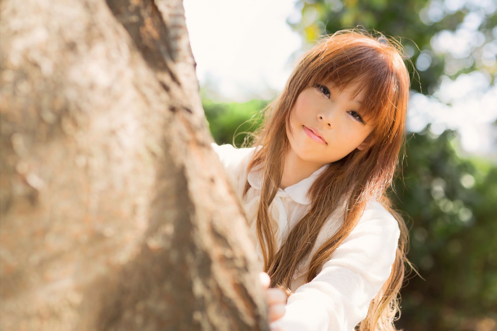 木陰で木の幹越しに覗く白シャツの女性［モデル：あみ］