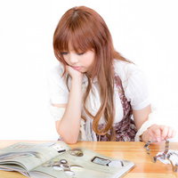 木製机で顎を支え雑誌を見る茶色い長い髪の女性の写真