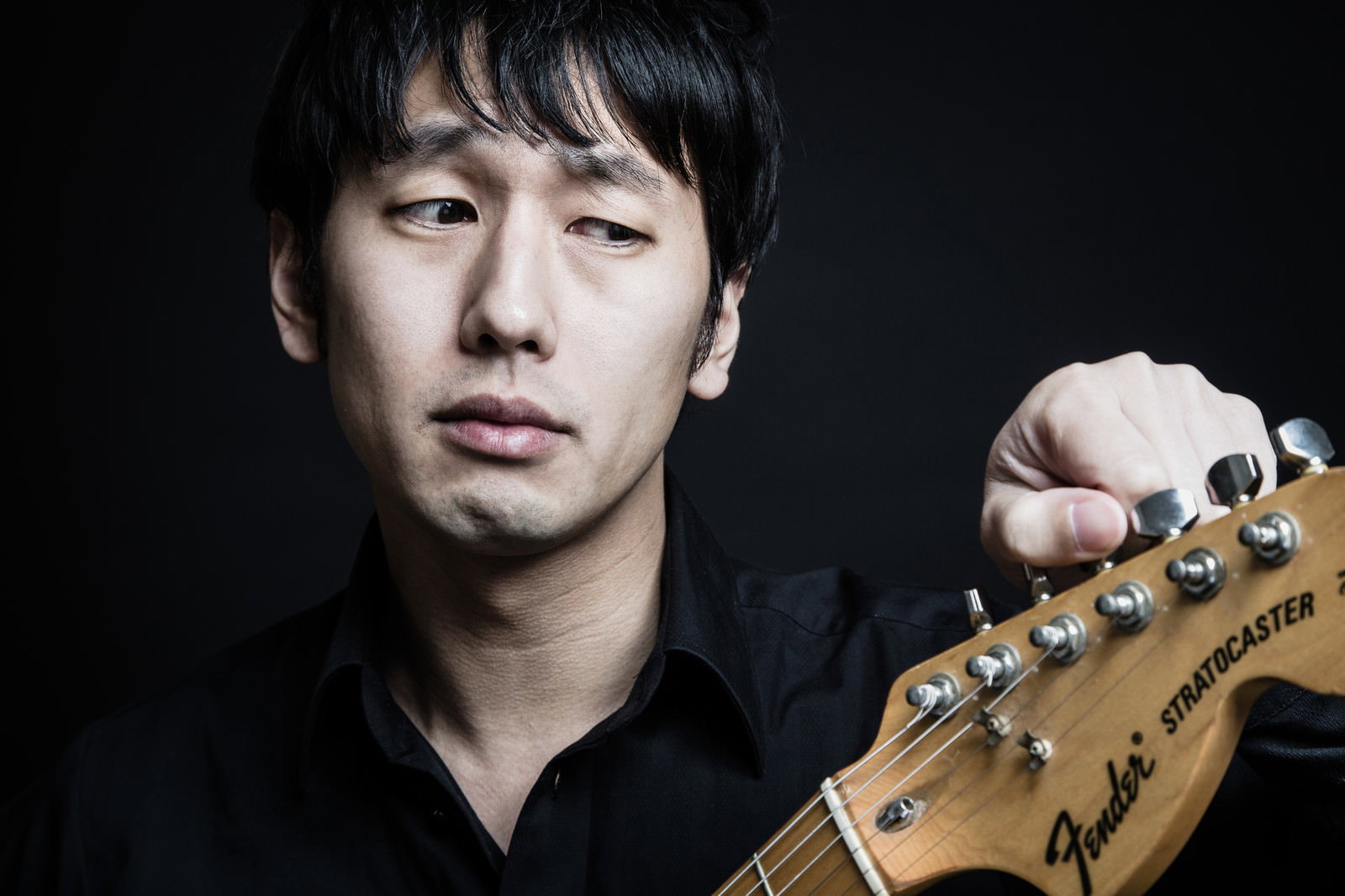 ストラトキャスターをチューニングする男性ギタリスト［モデル：大川竜弥］