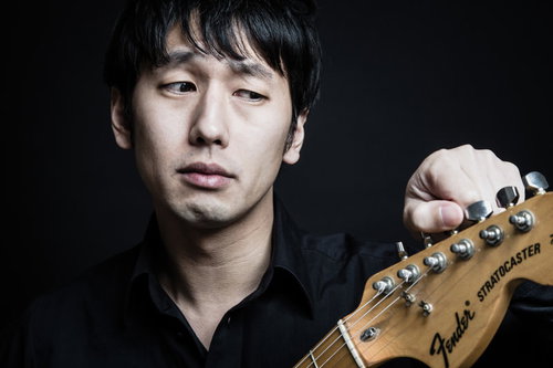 黒いシャツを着たギタリストがストラトキャスターをチューニング