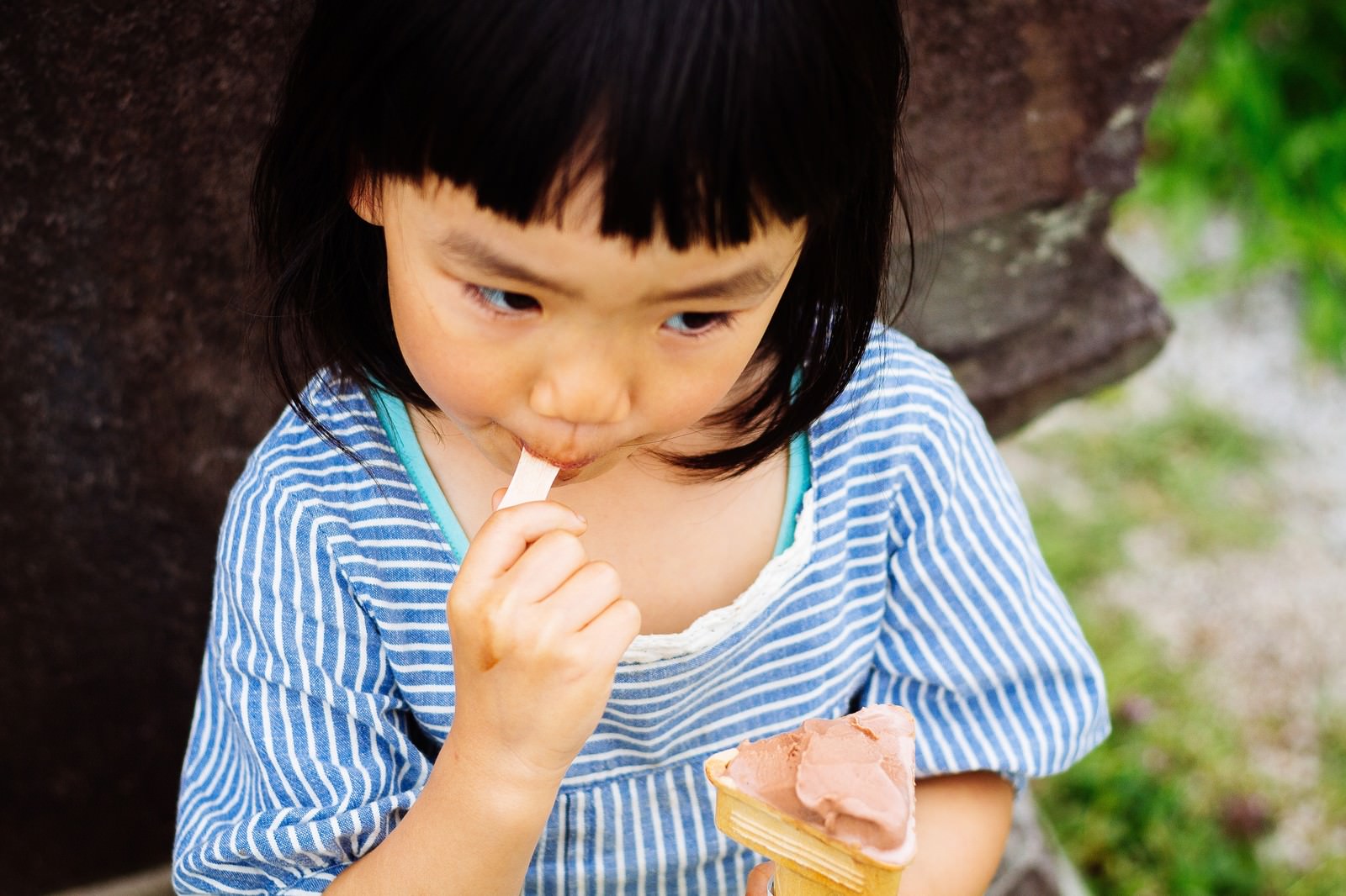樹木の前でアイスクリームをなめる女の子［モデル：あんじゅ］