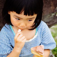 アイスクリームをペロリと食べる女の子、青白ストライプシャツ姿の写真