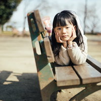待ちぼうけ少女がベンチで頬杖をつく公園の風景の写真