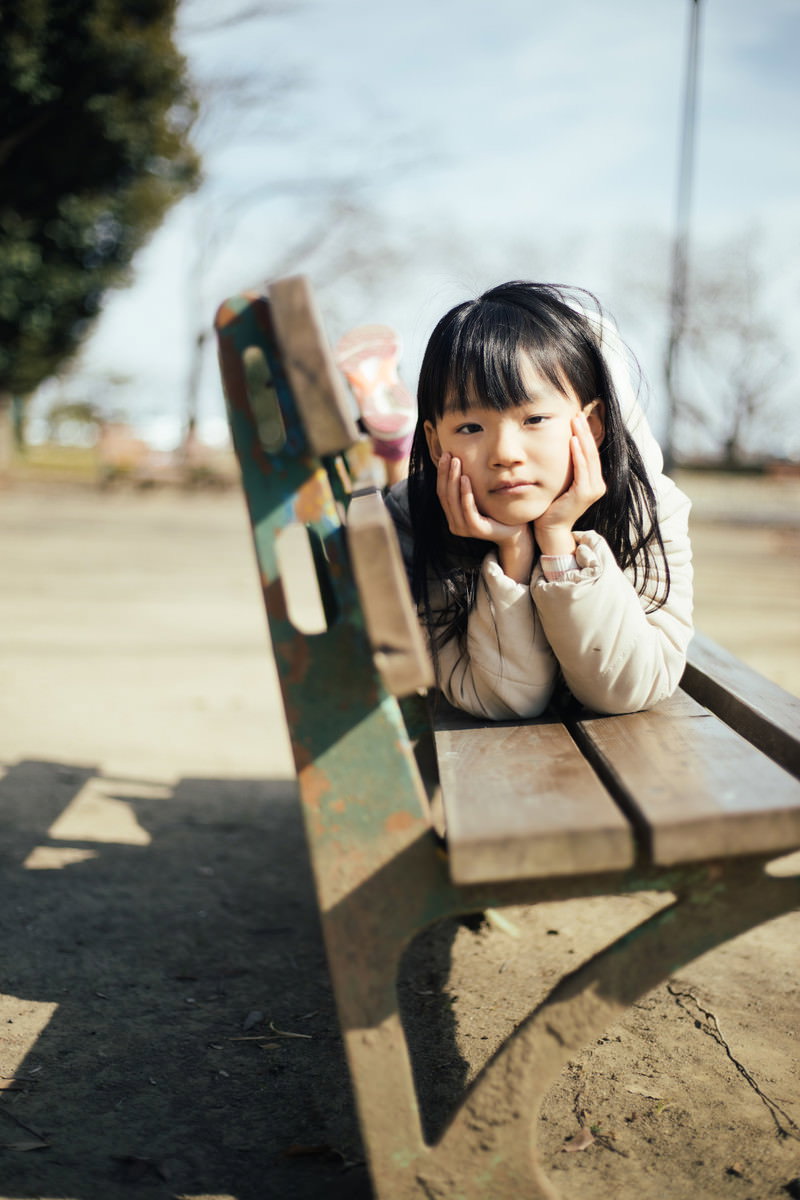 公園のベンチに座り頬杖をついて退屈そうな表情の女の子［モデル：あんじゅ］