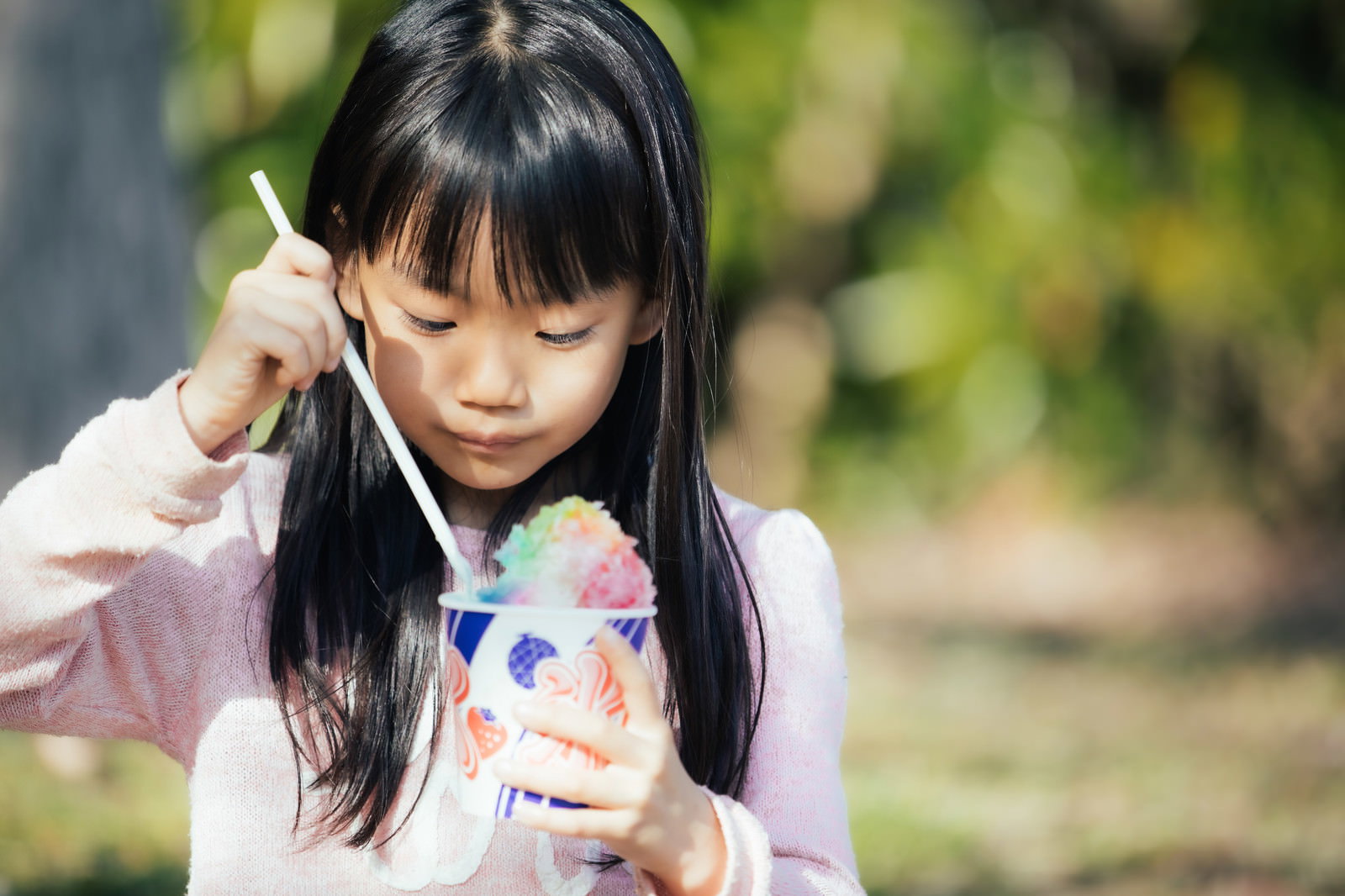 ピンクの服を着た女の子がカラフルなかき氷を食べている様子［モデル：あんじゅ］