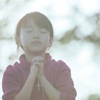 光の中で両手を合わせて祈るクリスチャンの少女の写真
