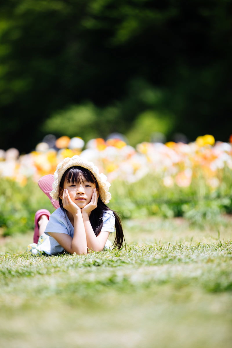 アイスランドポピーの花畑前で麦わら帽子をかぶり芝生でくつろぐ女の子［モデル：あんじゅ］