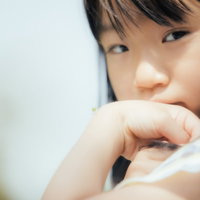 バッタの赤ちゃんを手首に乗せてじっと見つめる少女の写真