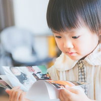 両手で雑誌を開いて見る縦縞シャツの黒髪ショートの幼児の写真