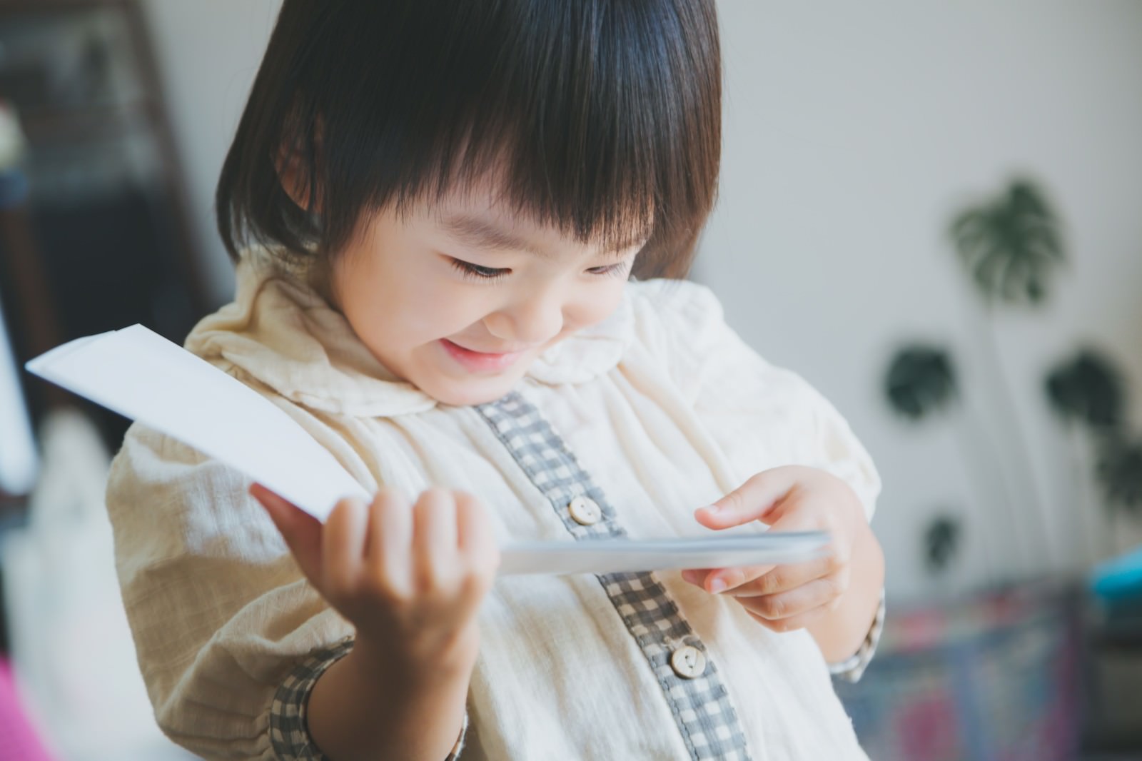 室内で紙飛行機を両手で持つ子供［モデル：あんじゅ］