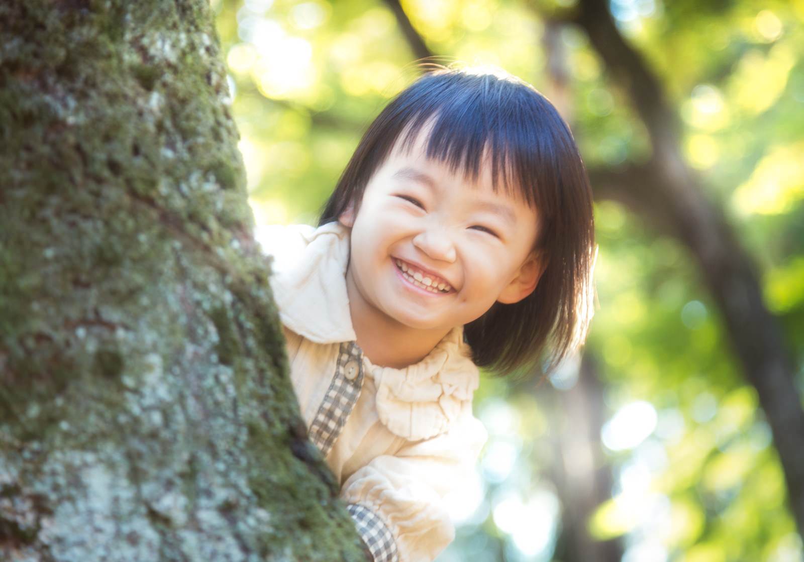 木の幹に寄りかかり笑顔を見せる格子柄の服の女の子［モデル：あんじゅ］