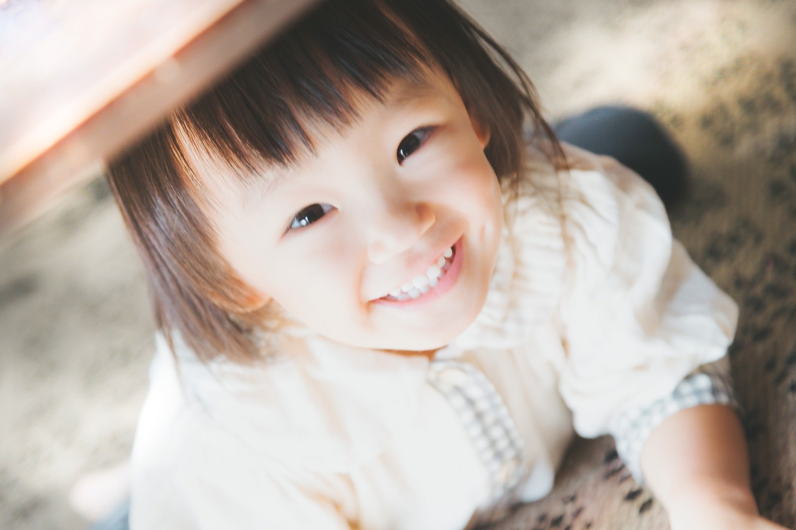 室内で上から見下ろして撮った白い服の笑顔の幼児［モデル：あんじゅ］