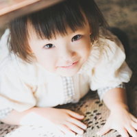 模様のある敷物の上で床に座る白い服の黒髪の子供の写真